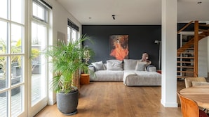 Ein modernes Wohnzimmer mit einem großen Fenster, einem grauen Sofa, einem Holzesstisch und einer Treppe.