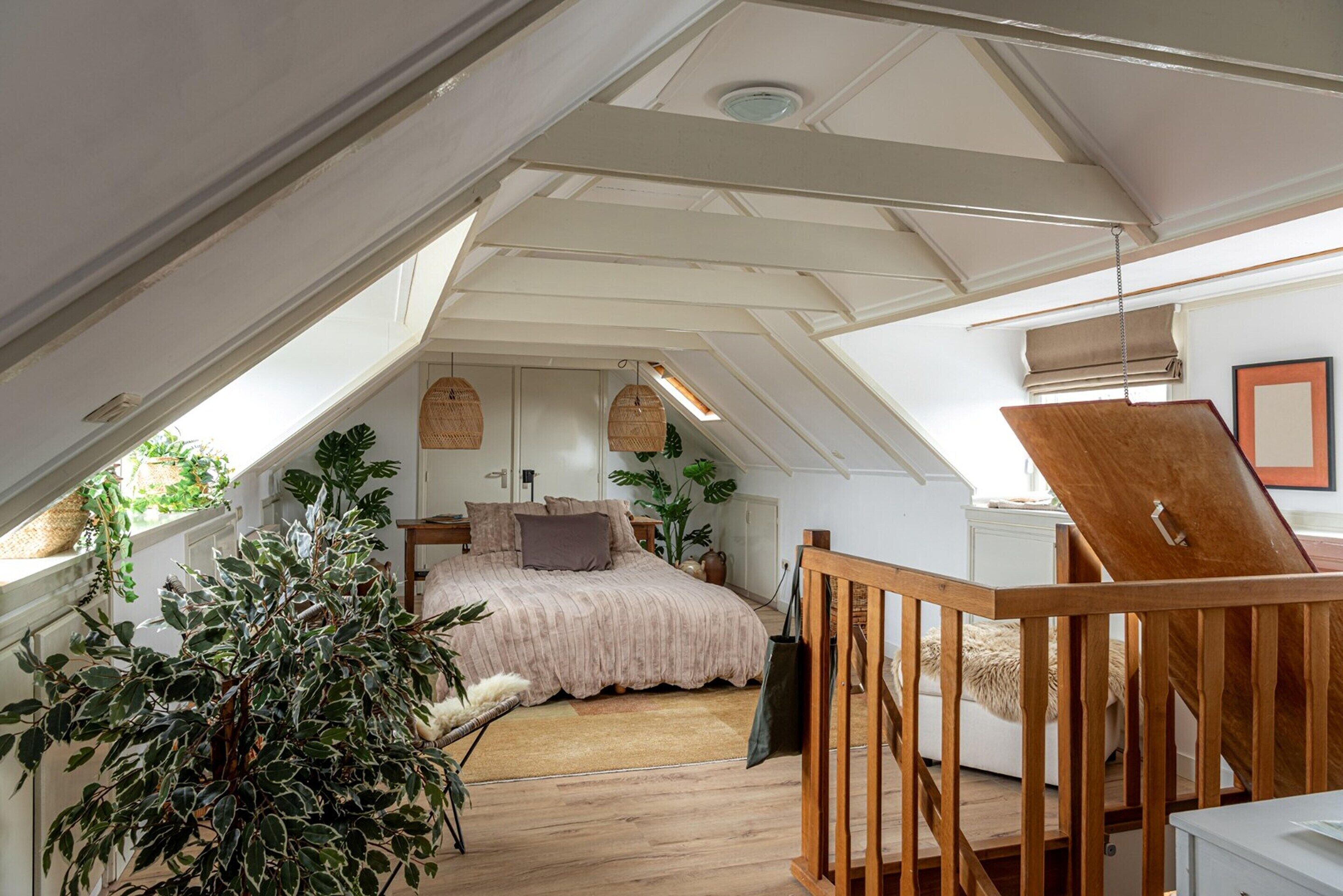 A bedroom with a sloped ceiling, a bed, a wooden chair, and a hanging light fixture.