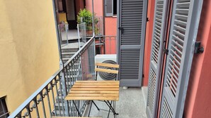 A narrow outdoor corridor with a wooden bench and tables, a metal railing, and a closed door. - Urban Loft Duomo - One Bedroom Apartment, Sleeps 2 (Alba)
