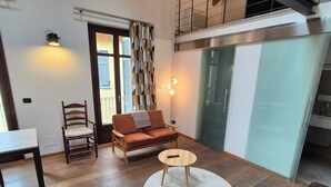 A modern living room with a wooden floor, a sofa, a chair, a small table, and a staircase leading to an upper level. - Urban Loft Duomo - One Bedroom Apartment, Sleeps 2 (Alba)
