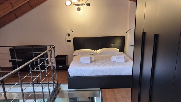 A modern bedroom with a glass ceiling, a bed with white linens, a black wardrobe, and a small table with a decorative item. - Urban Loft Duomo - One Bedroom Apartment, Sleeps 2 (Alba)