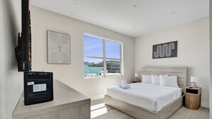 Une chambre d’hôtel avec un grand lit, une télévision, une fenêtre donnant sur un beau paysage et des œuvres d’art accrochées aux murs.