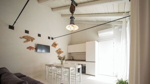 A modern living room with a sofa, dining table, chairs, and a TV. - Dimora Limonio -Damare- Pellestrina Ve (Venezia)
