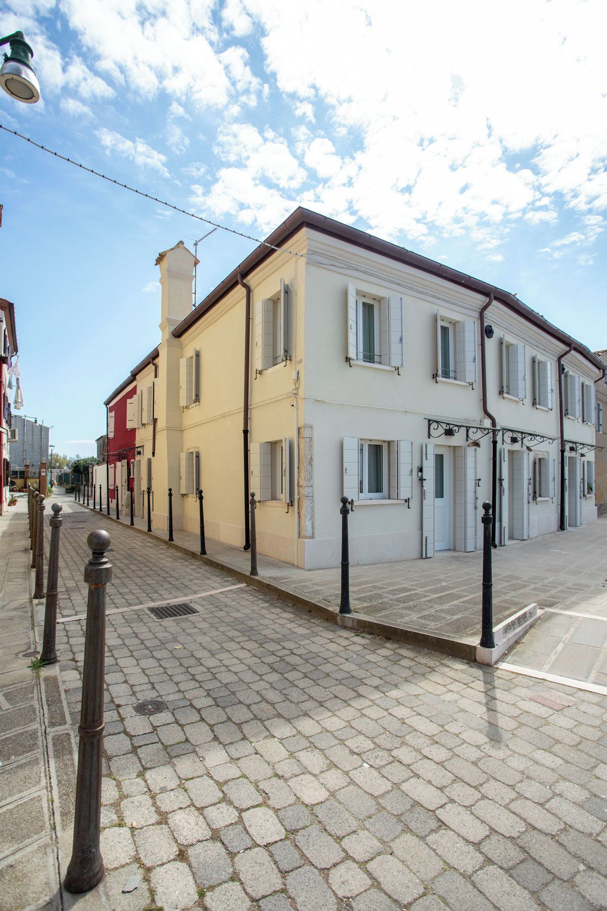 Una strada con pavimentazione in pietra, un edificio con numerose finestre e persiane, e un lampione.