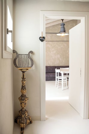Un corridoio con un elegante supporto metallico, una porta che dà su una stanza con un divano e un tavolo, e un lampadario.
