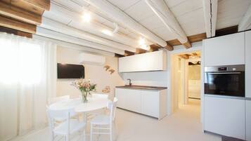A modern kitchen with white cabinetry, a built-in oven, and a dining area with a white table and chairs.