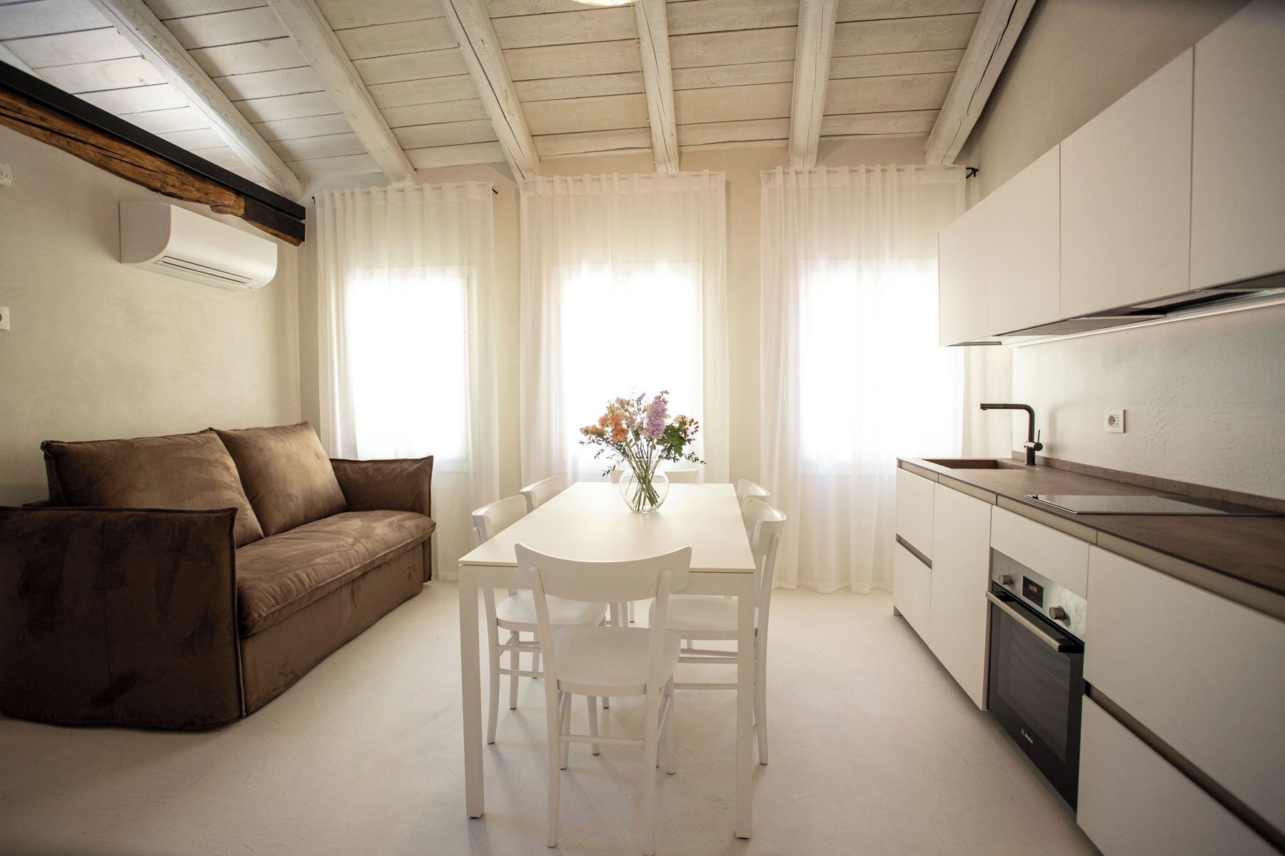 Una cocina moderna con comedor, muebles blancos y horno empotrado.