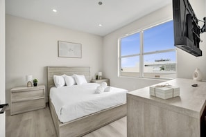 A modern bedroom with a large bed, bedside tables, a TV mounted on the wall, and a window with a city view.