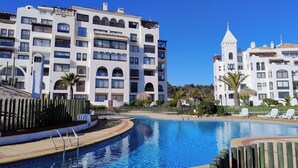 Een resort met een zwembad, witte gebouwen met balkons en palmbomen.