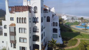 A large, white, multi-story building with a prominent tower, multiple windows, and a well-maintained lawn with a pool. - Spectacular ocean view, tranquility in a beautifully decorated apartment (Mirasol)