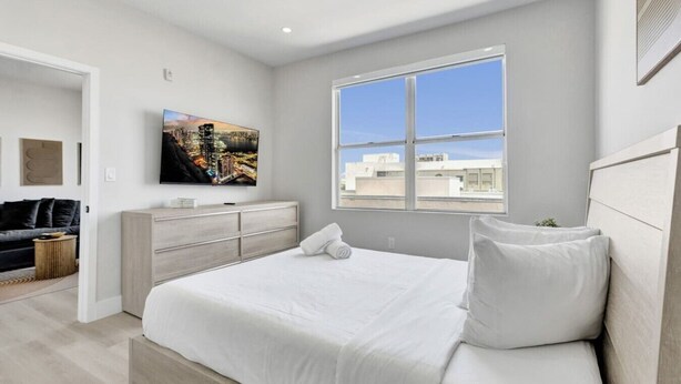 Une chambre moderne avec un grand lit, un téléviseur à écran plat, une commode et une fenêtre donnant sur la ville.