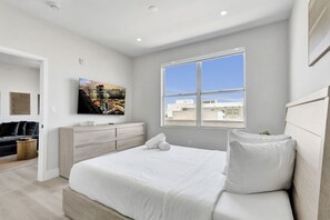 A modern bedroom with a large bed, a flat-screen TV, a dresser, and a window with a city view. - Modern 2 BDR South Beach Condo by Ocean Drive 404 (Miami Beach)
