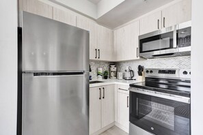 Une cuisine moderne dotée d’appareils électroménagers en acier inoxydable, de meubles de rangement en bois clair et d’un dosseret de carrelage disposé en motif chevrons.