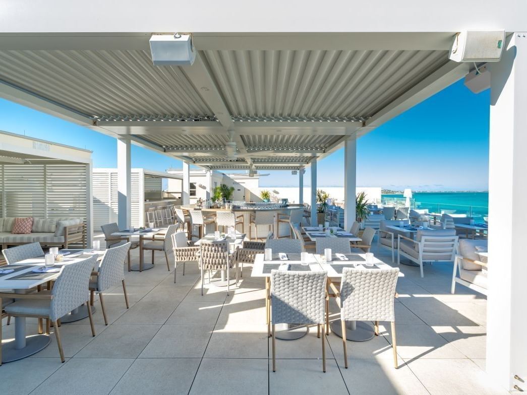 Un espace extérieur aménagé avec des tables et des chaises, un coin salon abrité et une vue sur l’océan.