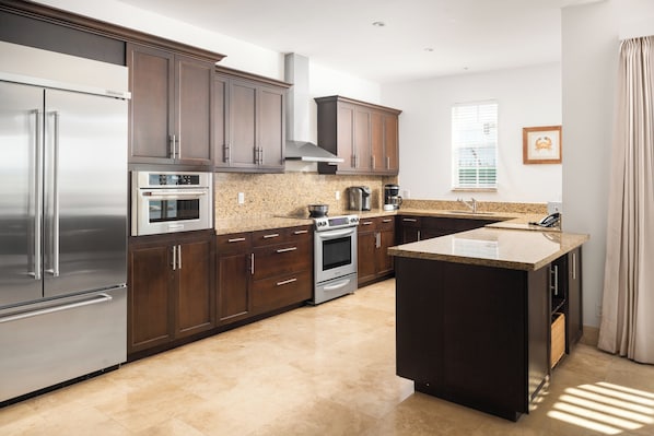 A modern kitchen with dark wood cabinets, stainless steel appliances, and a granite countertop. - Rooftop Villa Collection (Providenciales)