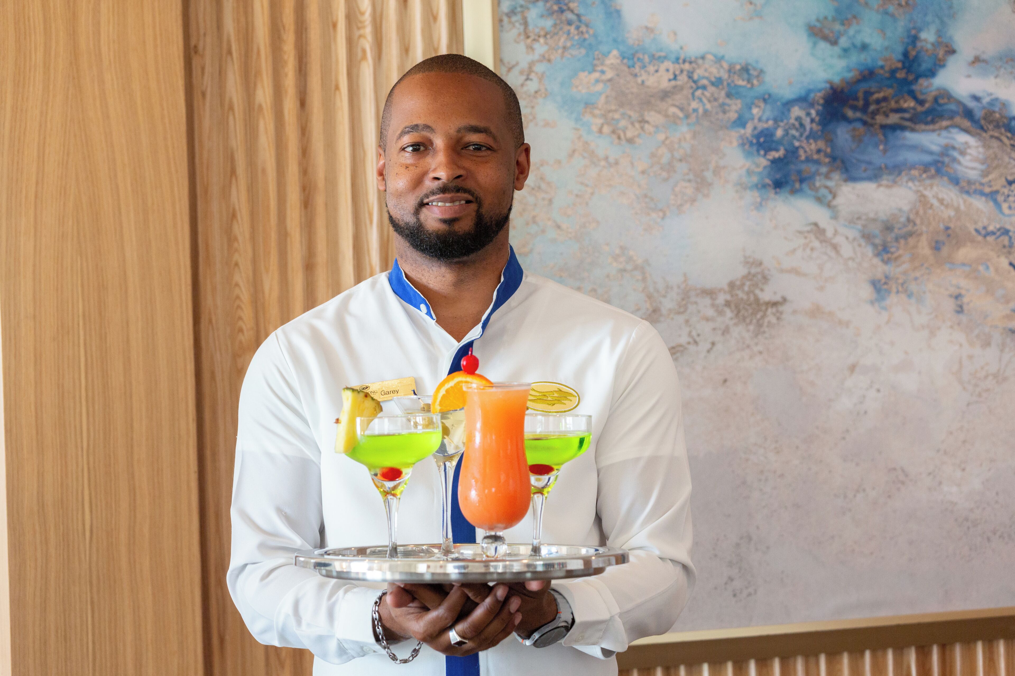 A person holding a tray with two cocktails and a fruit drink.