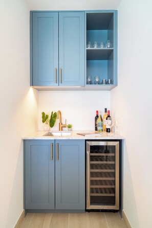 Une cuisine avec des meubles de couleur bleue, un évier, un réfrigérateur à vin et une plante.