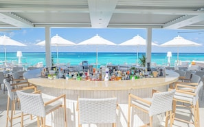 A bar area with a view of the ocean, featuring a bar counter, chairs, and umbrellas. - Rooftop Villa Collection (Providenciales)