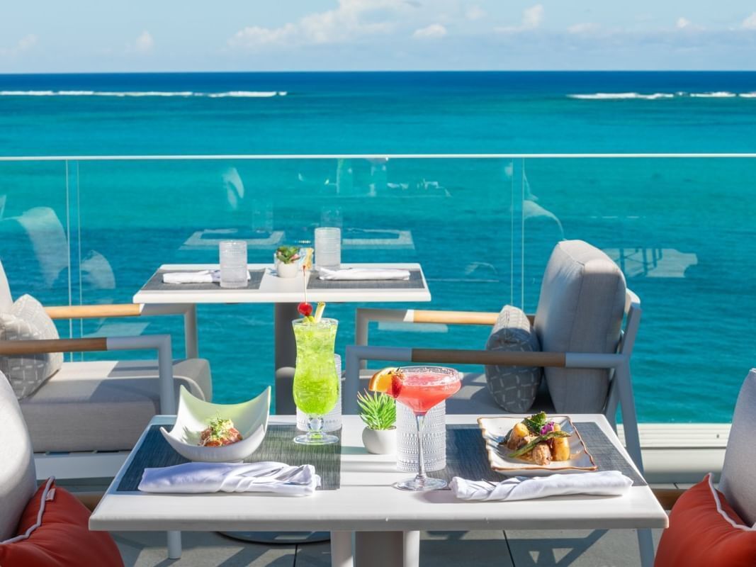 A dining table with a view of the ocean, a cocktail, and a meal.
