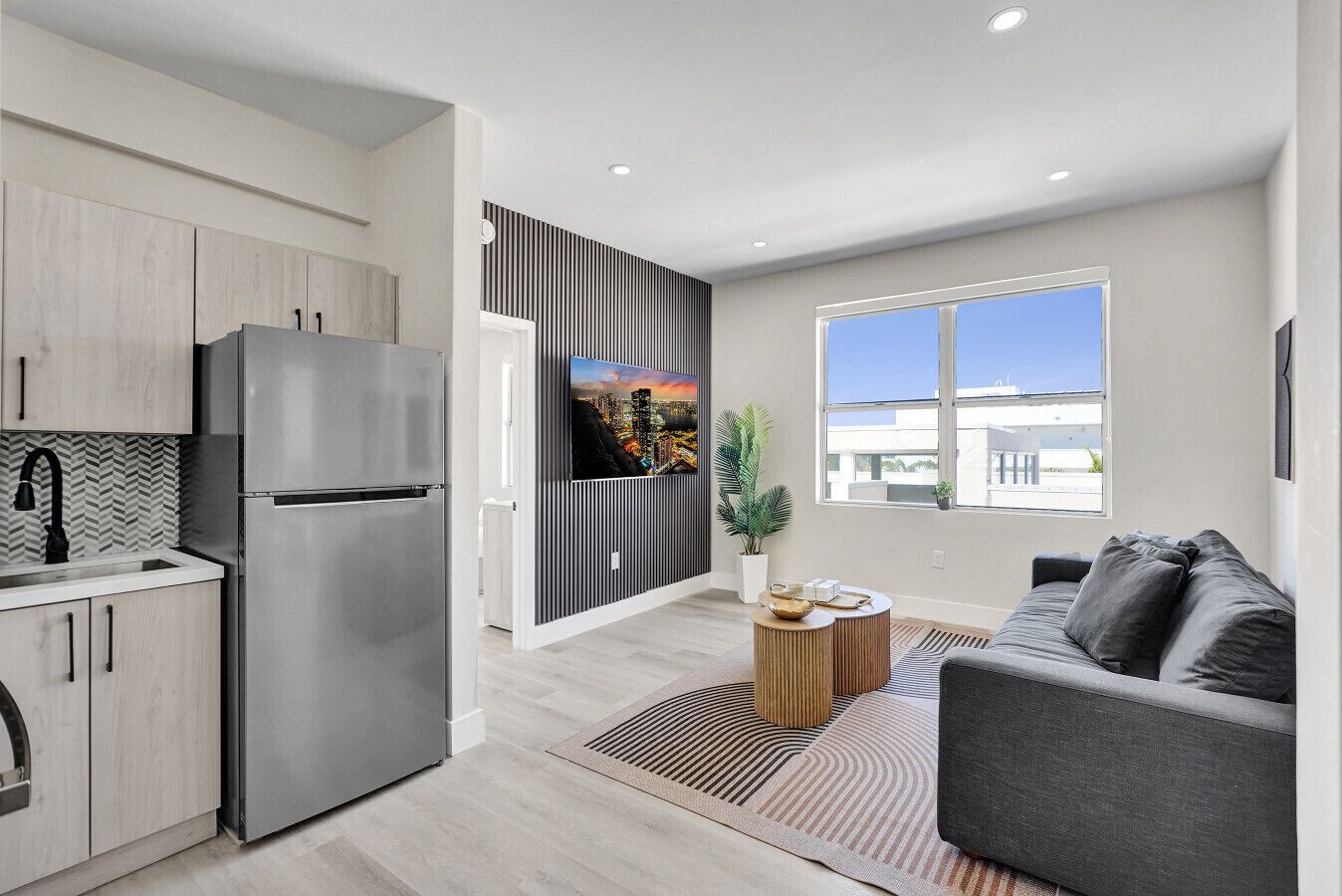 A modern kitchen with a stainless steel refrigerator, a herringbone-patterned backsplash, and a large window.