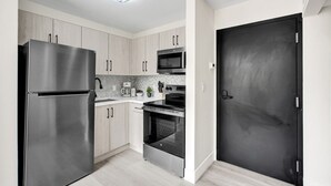 Una cocina moderna con electrodomésticos de acero inoxidable, armarios de madera clara y una puerta negra.