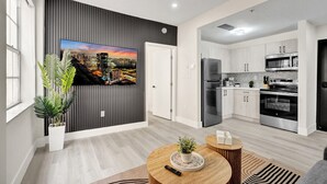 Une cuisine moderne équipée d’appareils électroménagers en acier inoxydable, un coin repas avec une table ronde et un grand tableau représentant un paysage urbain accroché au mur.
