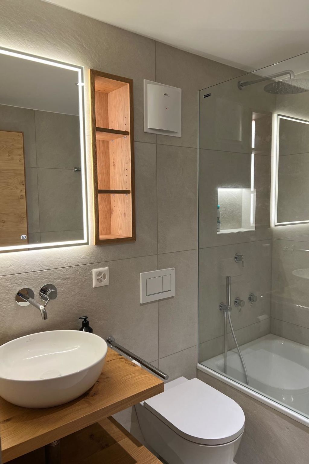 Une salle de bain moderne avec un grand miroir, un meuble-lavabo en bois, un lavabo blanc, des toilettes et une douche à parois de verre.