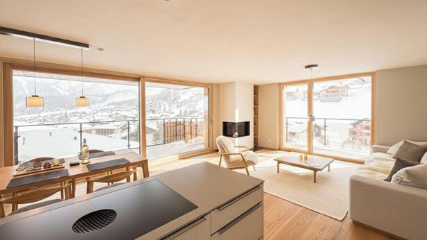 Ein modernes Wohnzimmer mit Essbereich, großen Fenstern und Blick auf eine verschneite Landschaft.