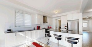 A modern kitchen with white cabinets, a large window, and a central island with bar stools. - Min 30 days Entire large 4bd house with 3 parking  (East Gwillimbury)