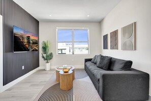 Uma sala de estar moderna com um sofá cinza, uma janela grande e uma pintura de paisagem urbana.