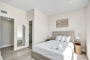Een moderne slaapkamer met een groot bed, een inloopkast en een gang naar een badkamer.