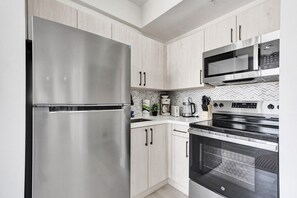 A modern kitchen with stainless steel appliances, light wood cabinetry, and a herringbone tile backsplash. - Chic 2 BDR Collins Gem 1 Min from the Ocean MLT (Miami Beach)
