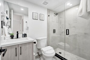 A modern bathroom with a glass shower enclosure, a white toilet, and a vanity with a mirror and sink. - Chic 2 BDR Collins Gem 1 Min from the Ocean MLT (Miami Beach)