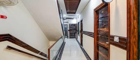 A hotel hallway with a marble floor, wooden doors, a fire exit sign, and a clock on the wall.