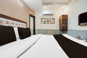 Quarto de hotel com uma cama grande, televisão de tela plana, aparelho de ar condicionado e quadros nas paredes.