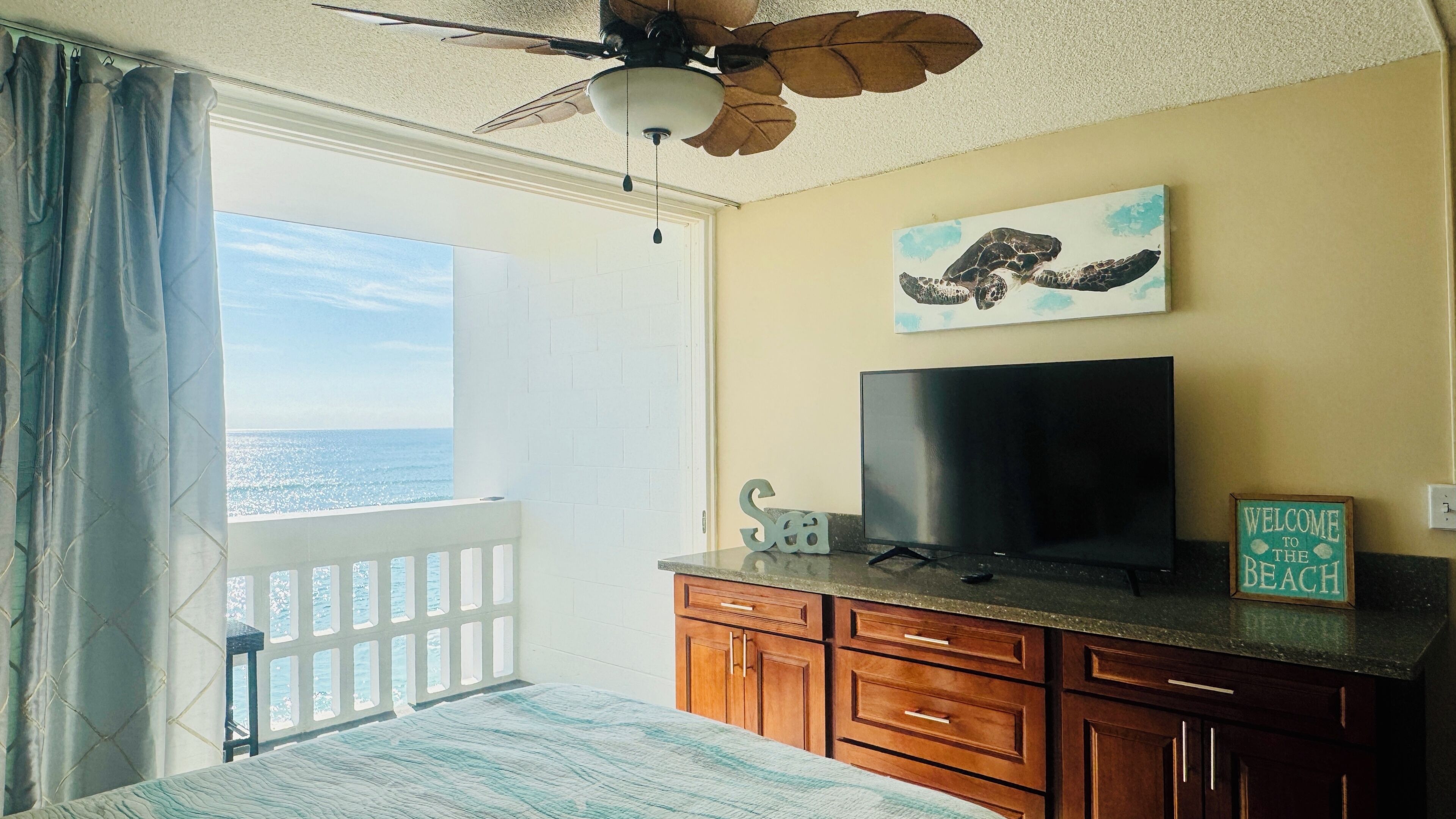 Ein Zimmer mit Balkon, Deckenventilator, Flachbildfernseher, Holzausstattung und einem Schild mit der Aufschrift 'Welcome to the Beach'.