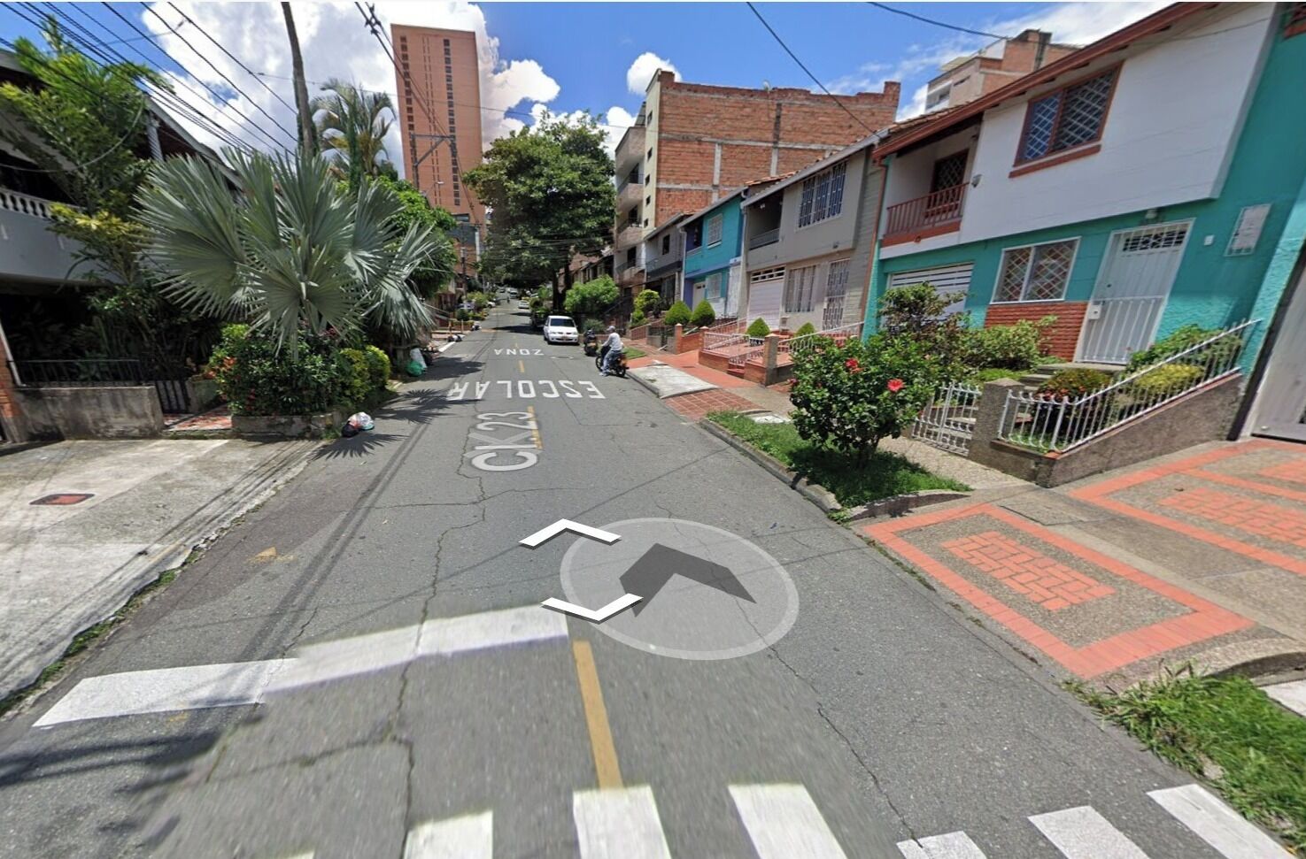 Una calle residencial con casas, una escuela y cielo despejado.