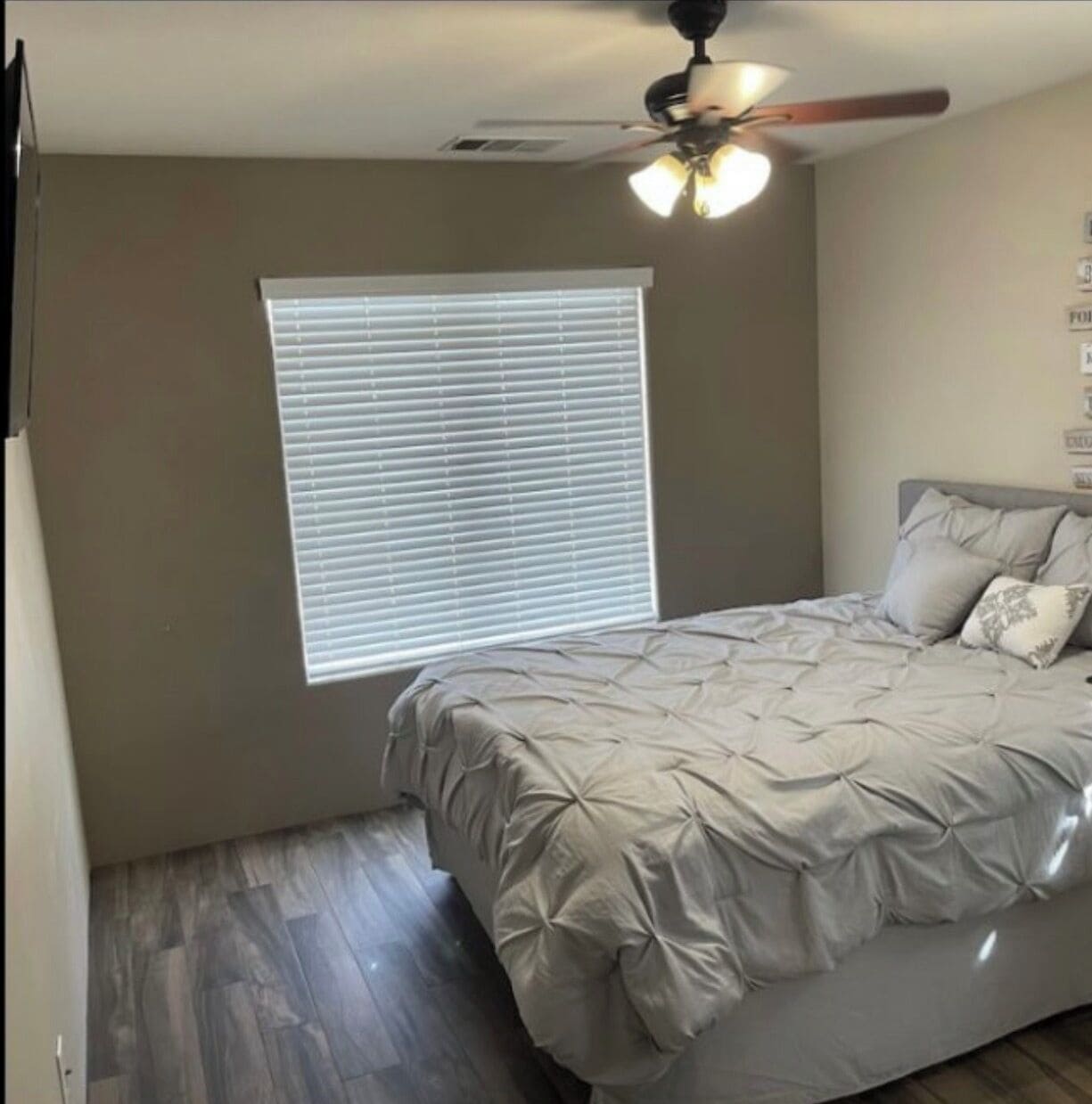 Un dormitorio con cama, ventilador de techo, ventana con persianas y suelo de madera.
