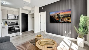 A modern living room with a flat-screen TV, a kitchen with appliances, and a large window. - Comfortable 1BR Apartment in Prime South Beach 307 (Miami Beach)