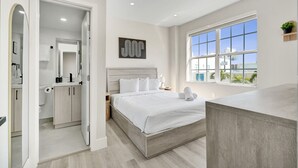 A modern bedroom with a large bed, a bathroom with a toilet and sink, and a window with a view of buildings. - Comfortable 1BR Apartment in Prime South Beach 307 (Miami Beach)