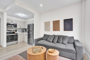 Ein modernes Wohnzimmer mit einem grauen Sofa, Holzbeistelltischen und einer Küche im Hintergrund.