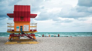 Ein Rettungsschwimmturm mit der Aufschrift 'MIAMI BEACH', der auf einem Sandstrand mit Blick aufs Meer steht.