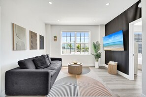 Un salon moderne avec un canapé gris, une table basse ronde et un grand téléviseur à écran plat fixé sur un panneau noir.