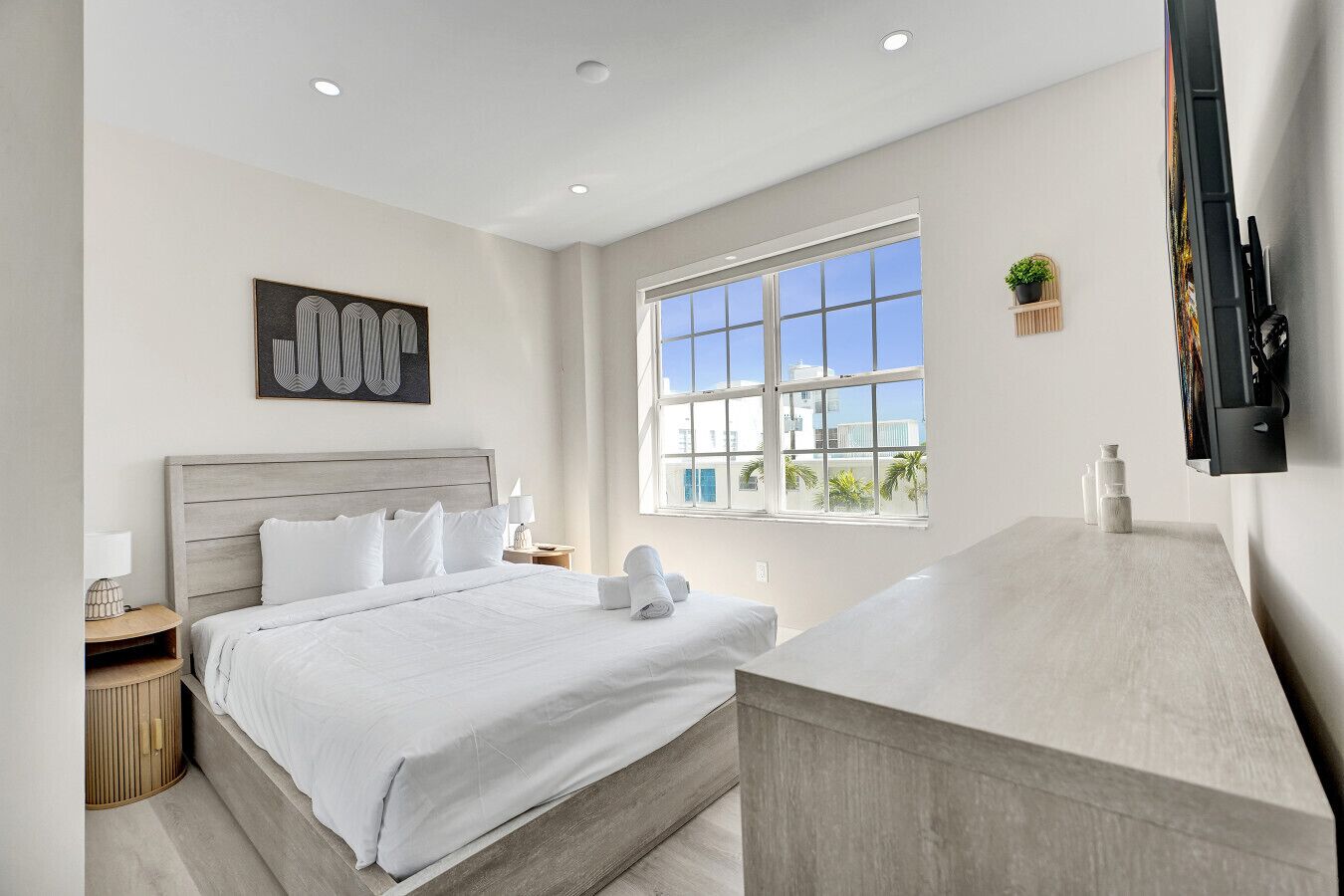 A modern hotel room with a large bed, a desk, a window with a view, and a mounted TV.