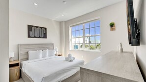 Una habitación de hotel moderna con una cama grande, un escritorio, una ventana con vistas y un televisor montado.