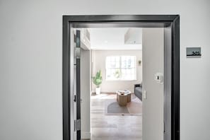 Ein modernes Interieur mit einer Tür mit der Aufschrift '305', einem großen Fenster, einer Topfpflanze und einem runden Tisch.