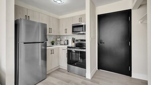 Una cucina moderna con elettrodomestici in acciaio inossidabile, mobili chiari in legno e una porta nera.