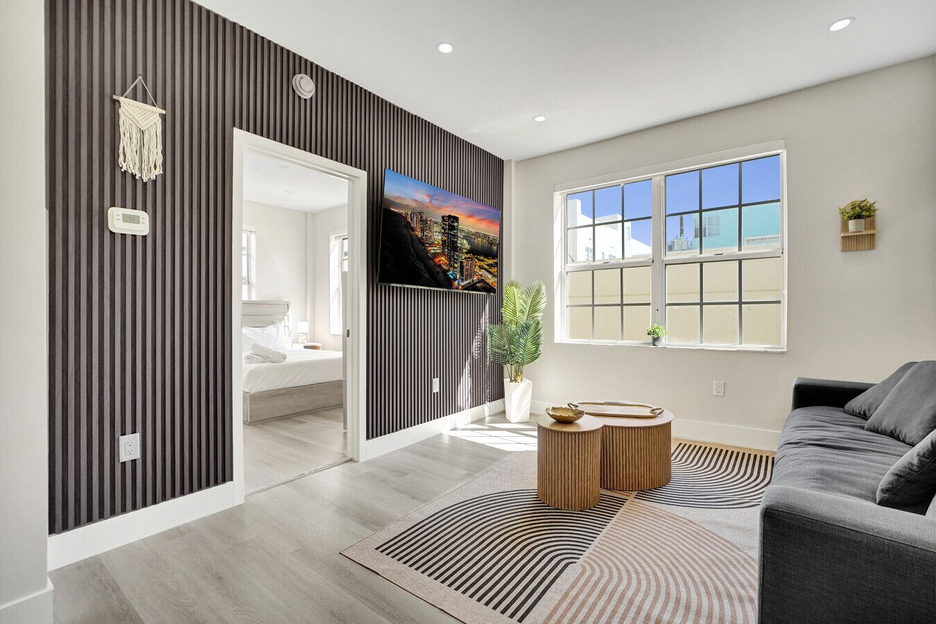 A modern living room with a large window, a flat-screen TV, a grey sofa, and a wooden coffee table.