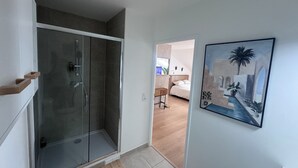 A modern bathroom with a glass-enclosed shower, a wooden bench, and a framed painting of a coastal scene. - ☀ El Cubanito | Studio 30 m² | Aéroport CDG – Paris ❤ (Villiers-le-Bel)
