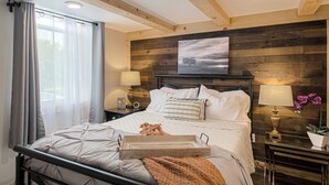 Un lit bien fait, avec une table d’appoint, une lampe de chevet et un tableau accroché au mur.